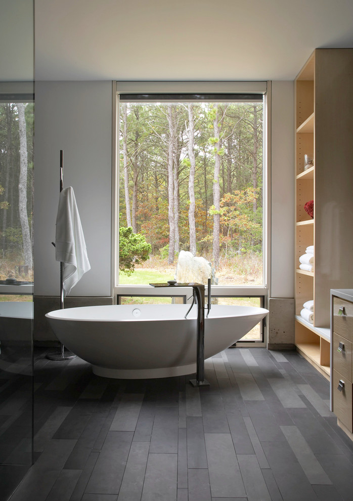 Modern master bathroom in New York with flat-panel cabinets, light wood cabinets, a freestanding tub and white walls.