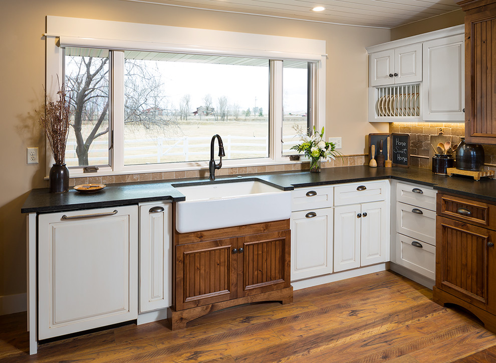 Large country l-shaped eat-in kitchen in Other with a farmhouse sink, flat-panel cabinets, white cabinets, granite benchtops, multi-coloured splashback, travertine splashback, stainless steel appliances, with island and black benchtop.