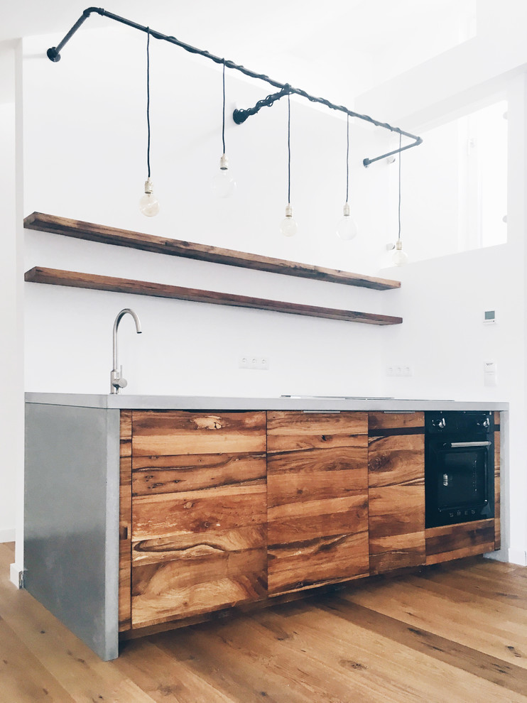 Photo of a mid-sized industrial single-wall open plan kitchen in Berlin with an integrated sink, flat-panel cabinets, medium wood cabinets, concrete benchtops, white splashback, black appliances and medium hardwood floors.
