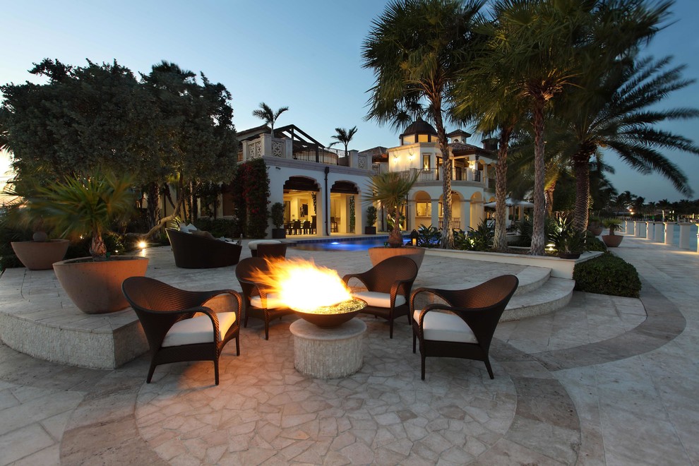 This is an example of an expansive mediterranean backyard patio in Miami with a fire feature, natural stone pavers and no cover.