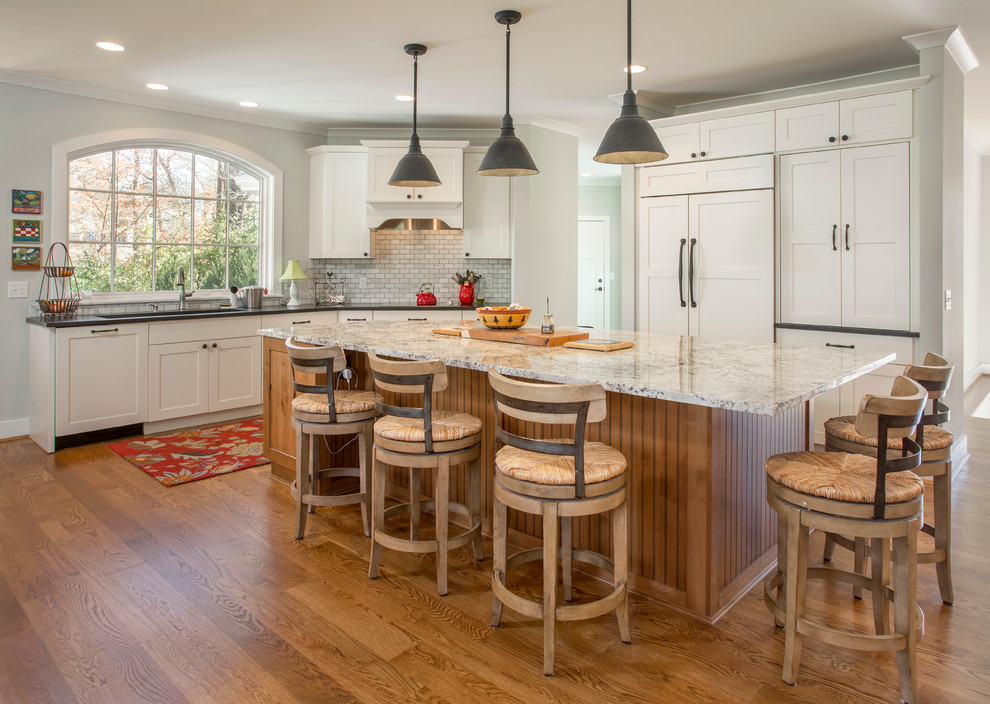 Inspiration for a large transitional l-shaped eat-in kitchen in Cincinnati with shaker cabinets, white cabinets, granite benchtops, grey splashback, stone tile splashback, panelled appliances, with island, medium hardwood floors, a double-bowl sink and brown floor.