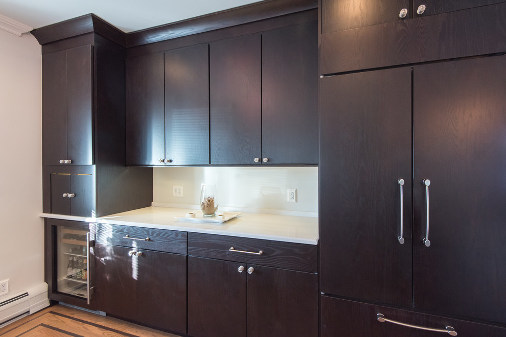 Photo of a mid-sized transitional single-wall wet bar in Atlanta with medium hardwood floors, no sink, flat-panel cabinets, dark wood cabinets, solid surface benchtops and white splashback.