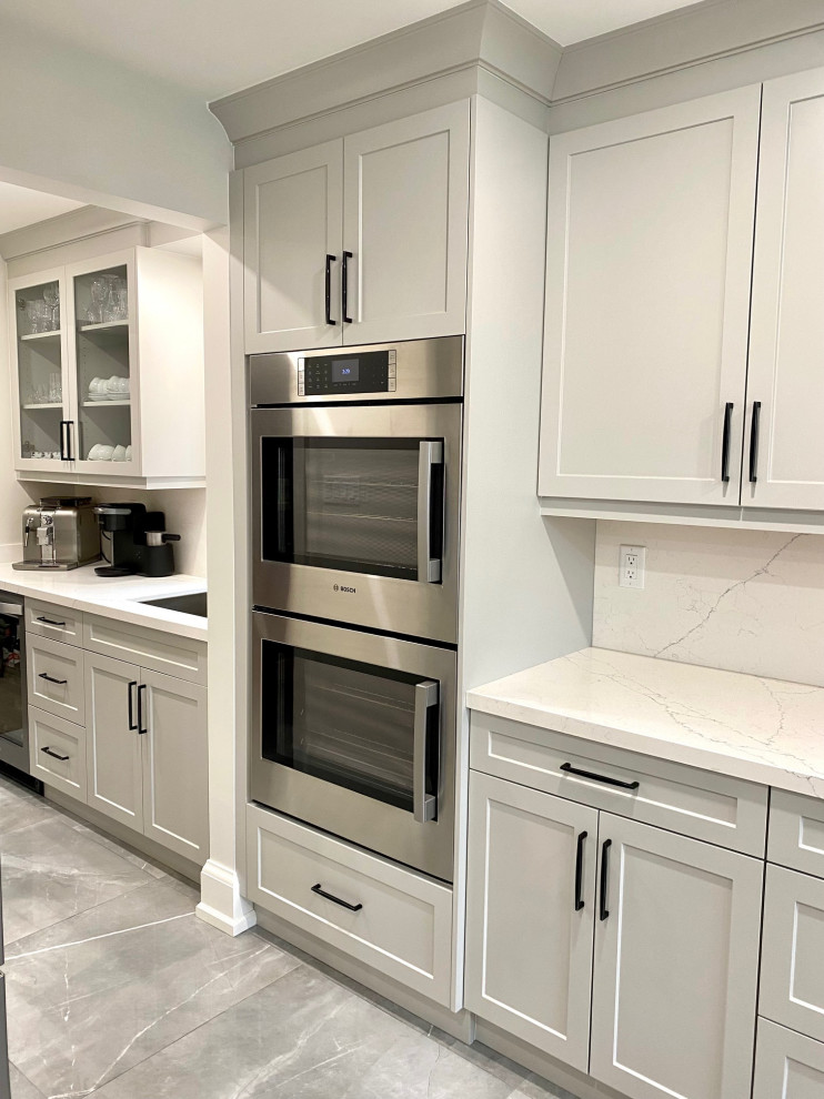 Mid-sized transitional l-shaped porcelain tile open concept kitchen photo in Toronto with an undermount sink, shaker cabinets, gray cabinets, quartz countertops, white backsplash, quartz backsplash, stainless steel appliances, an island and white countertops