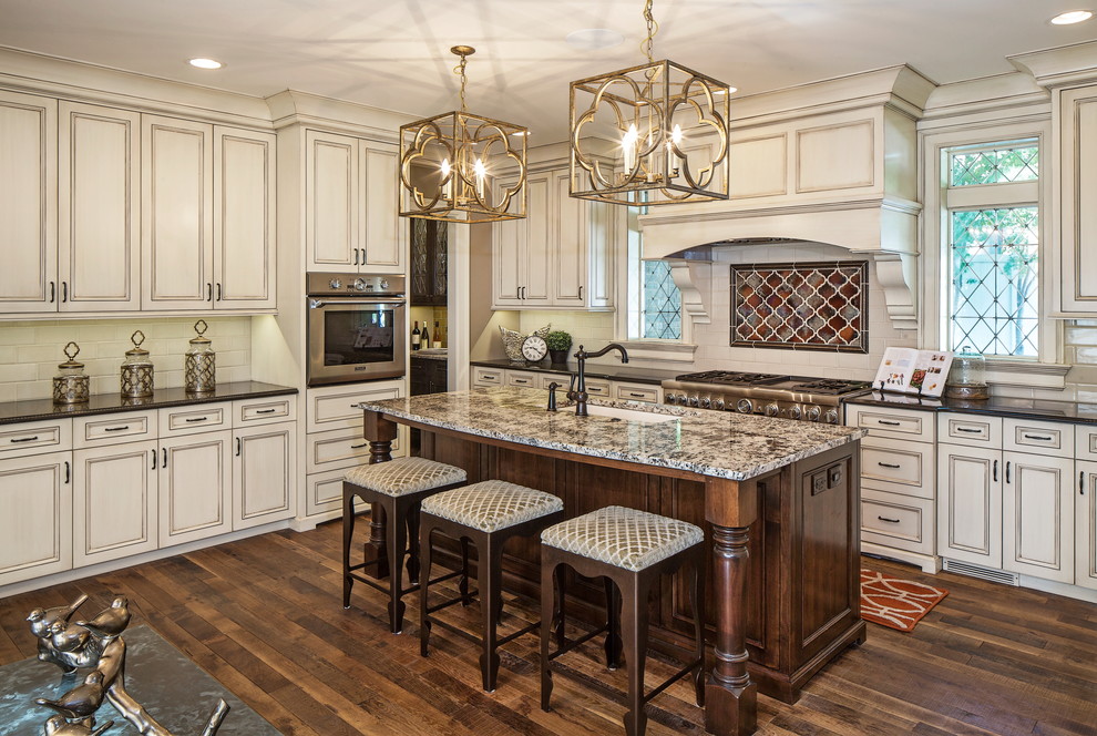 Photo of a large traditional u-shaped separate kitchen in Omaha with an undermount sink, beaded inset cabinets, beige cabinets, granite benchtops, white splashback, subway tile splashback, stainless steel appliances, medium hardwood floors, with island and brown floor.