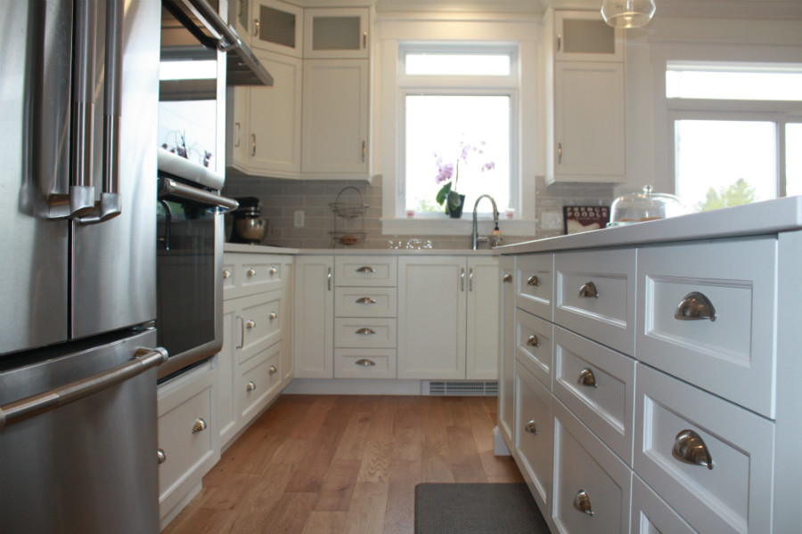 Mid-sized transitional l-shaped medium tone wood floor kitchen pantry photo with an undermount sink, shaker cabinets, white cabinets, quartz countertops, gray backsplash, cement tile backsplash, stainless steel appliances, an island and white countertops