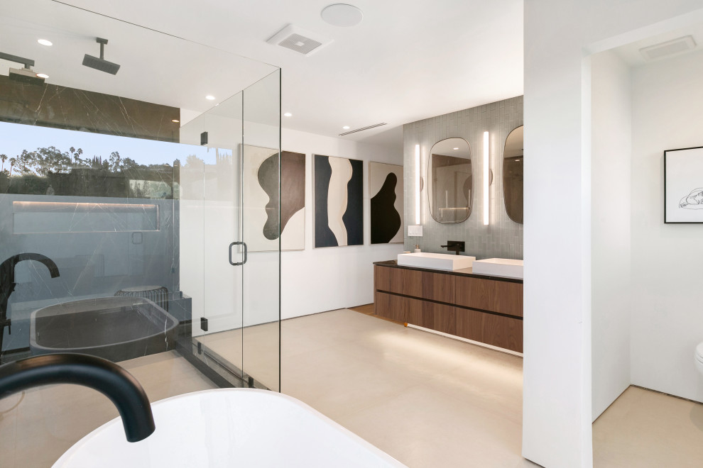 This is an example of a large contemporary master bathroom in Los Angeles with flat-panel cabinets, medium wood cabinets, a freestanding tub, a corner shower, porcelain floors, a trough sink, marble benchtops, a hinged shower door and black benchtops.