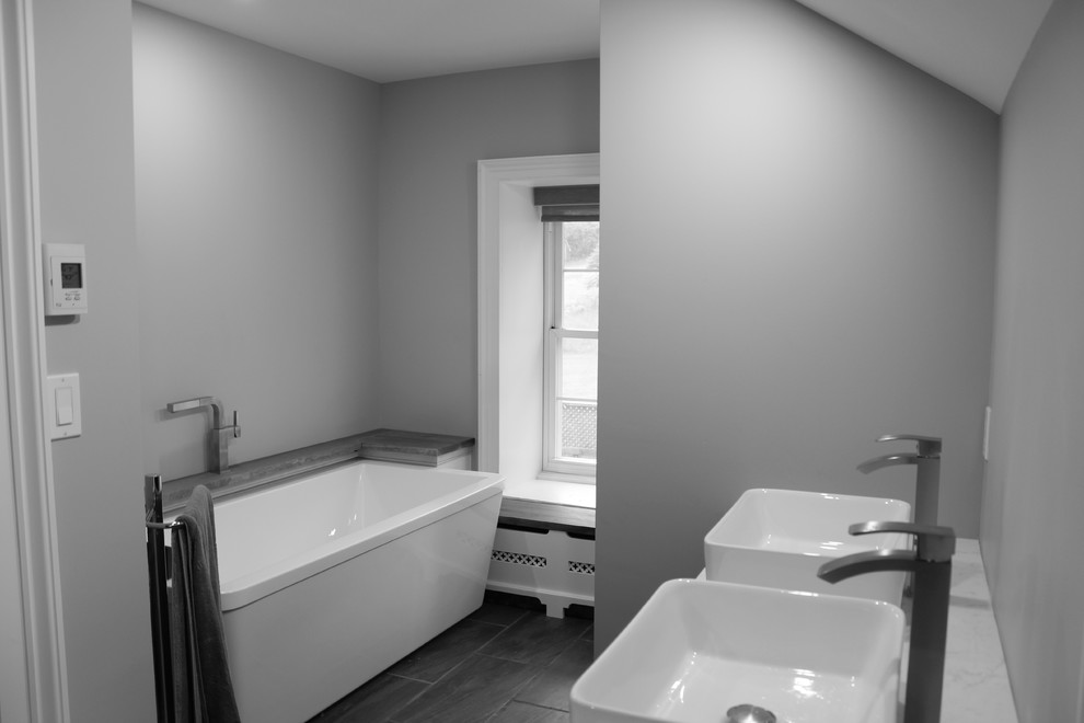 Design ideas for a mid-sized traditional master bathroom in Toronto with shaker cabinets, dark wood cabinets, a freestanding tub, a bidet, gray tile, ceramic tile, grey walls, porcelain floors, a console sink, engineered quartz benchtops, grey floor and a hinged shower door.