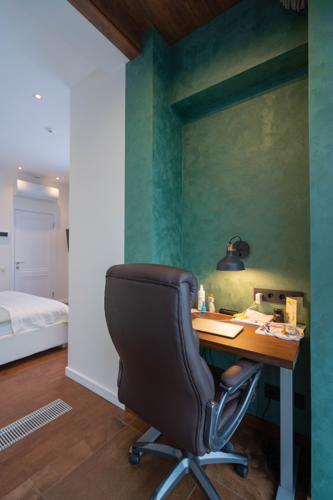 Immagine di una piccola stanza da lavoro minimal con pareti verdi, pavimento in sughero, scrivania incassata e pavimento marrone
