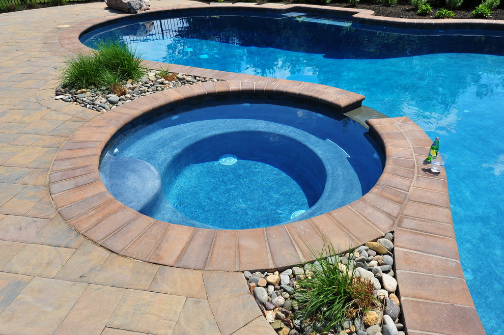 Inspiration for a mid-sized traditional backyard custom-shaped pool in New York with a hot tub and concrete pavers.