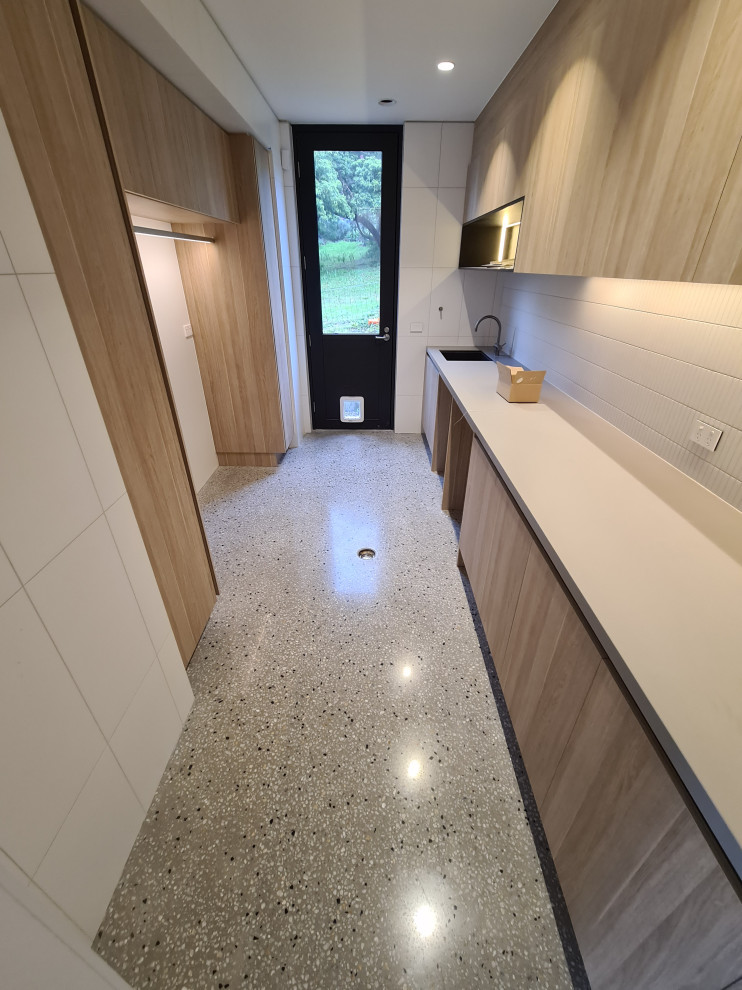 Inspiration for a medium sized contemporary galley separated utility room in Melbourne with a submerged sink, flat-panel cabinets, light wood cabinets, quartz worktops, white splashback, matchstick tiled splashback, white walls, concrete flooring, a side by side washer and dryer, grey floors and white worktops.