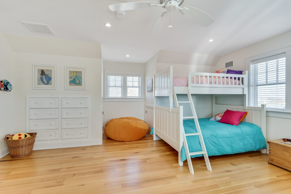 Photo of a large beach style gender-neutral kids' bedroom in New York with white walls and light hardwood floors.