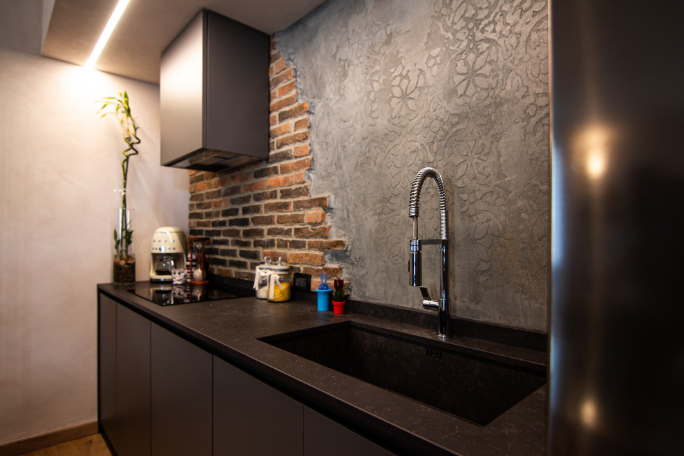 Inspiration for a small industrial single-wall open plan kitchen in Milan with an integrated sink, flat-panel cabinets, grey cabinets, brick splashback, stainless steel appliances, laminate floors, no island and black benchtop.
