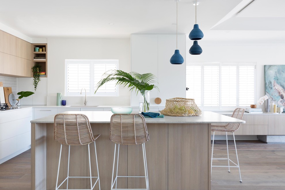 Design ideas for a mid-sized beach style l-shaped eat-in kitchen in Sydney with an undermount sink, flat-panel cabinets, white cabinets, white splashback, light hardwood floors, with island, beige floor and white benchtop.