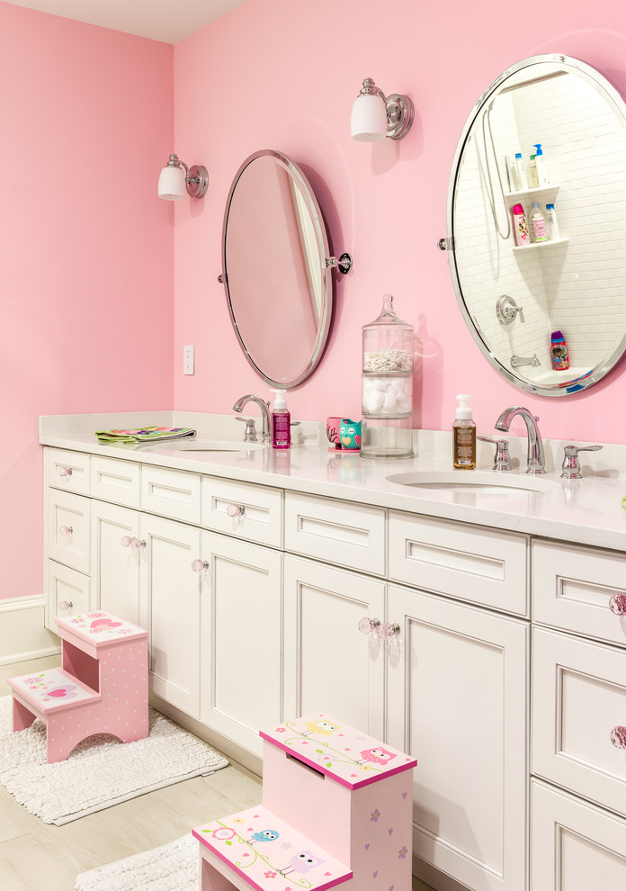 This is an example of a traditional kids bathroom in New York with recessed-panel cabinets, white cabinets, pink walls and an undermount sink.