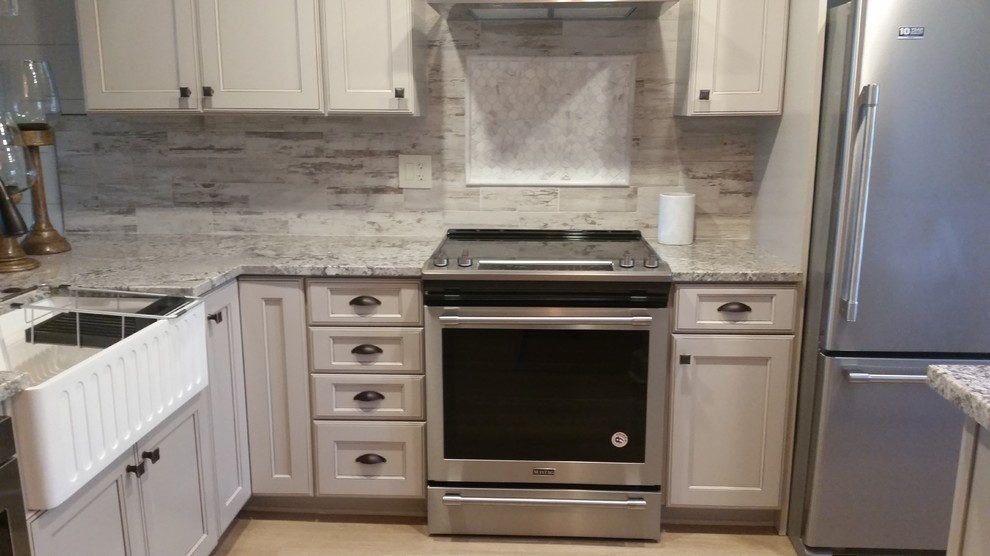 Photo of a small country l-shaped separate kitchen in Tampa with a farmhouse sink, shaker cabinets, beige cabinets, granite benchtops, white splashback, ceramic splashback, stainless steel appliances, laminate floors, a peninsula and beige floor.