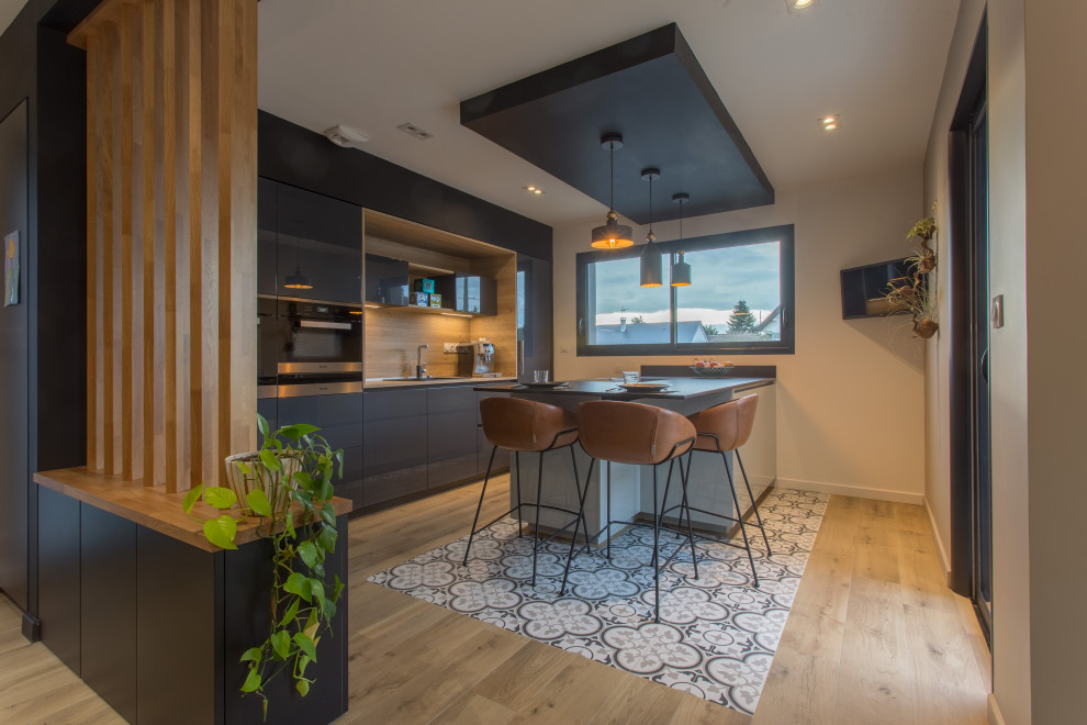 Photo of a contemporary galley kitchen in Other with an undermount sink, flat-panel cabinets, grey cabinets, black appliances, light hardwood floors, a peninsula, beige floor and beige benchtop.