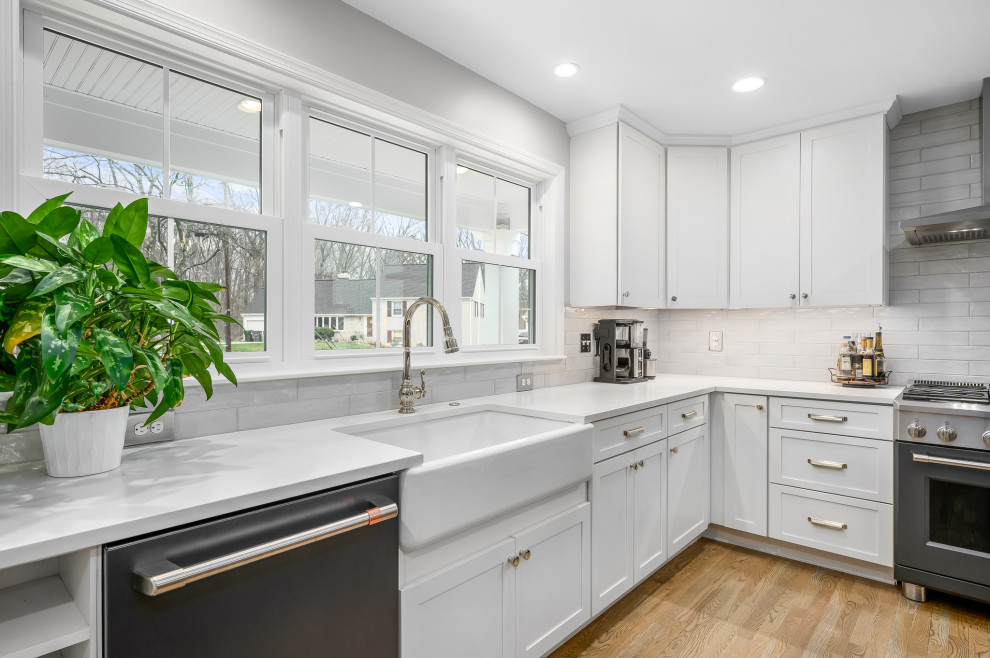 Design ideas for a traditional l-shaped kitchen in DC Metro with a belfast sink, shaker cabinets, white cabinets, engineered stone countertops, white splashback, ceramic splashback, medium hardwood flooring, an island, brown floors and white worktops.