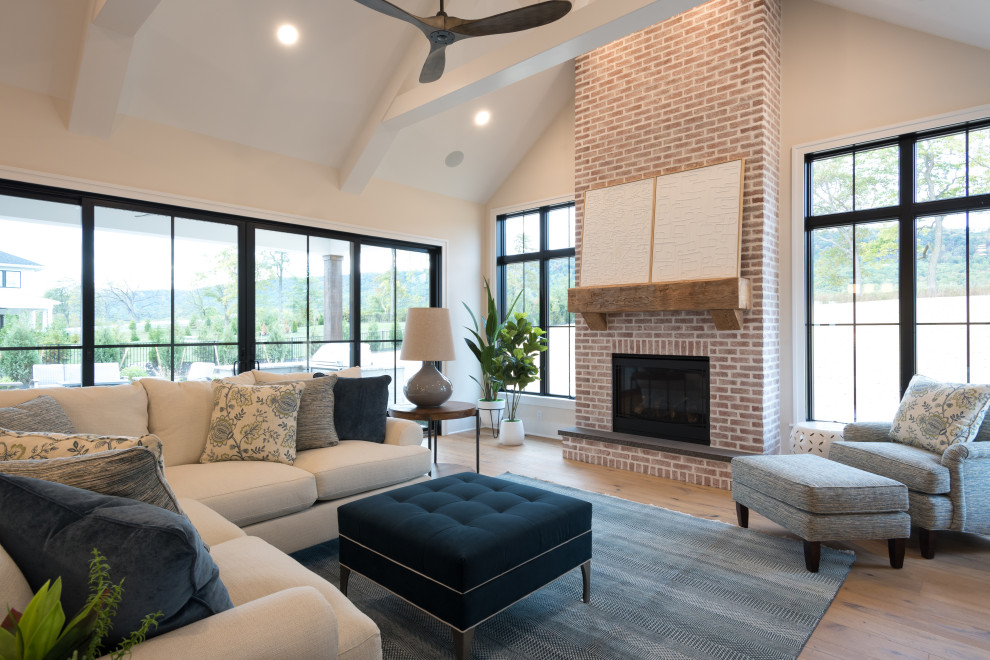 This is an example of an expansive rural open plan living room in Other with white walls, medium hardwood flooring, a standard fireplace, a brick fireplace surround, a built-in media unit, brown floors and a vaulted ceiling.