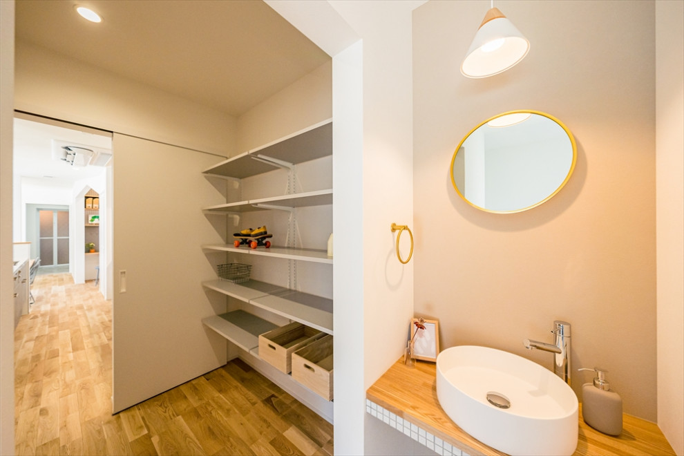 Photo of a modern powder room in Other with open cabinets, white cabinets, medium hardwood floors, a drop-in sink, tile benchtops, a built-in vanity and wallpaper.