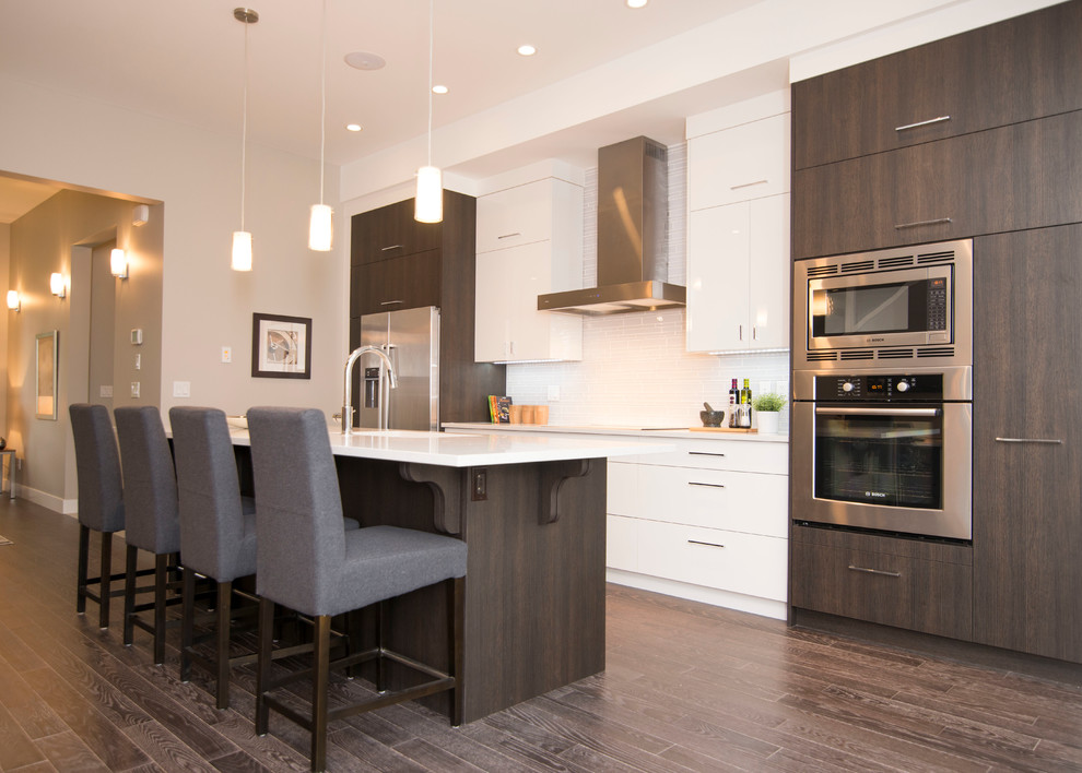 Design ideas for a large contemporary galley open plan kitchen in Calgary with an undermount sink, flat-panel cabinets, white cabinets, white splashback, mosaic tile splashback, stainless steel appliances, medium hardwood floors and with island.