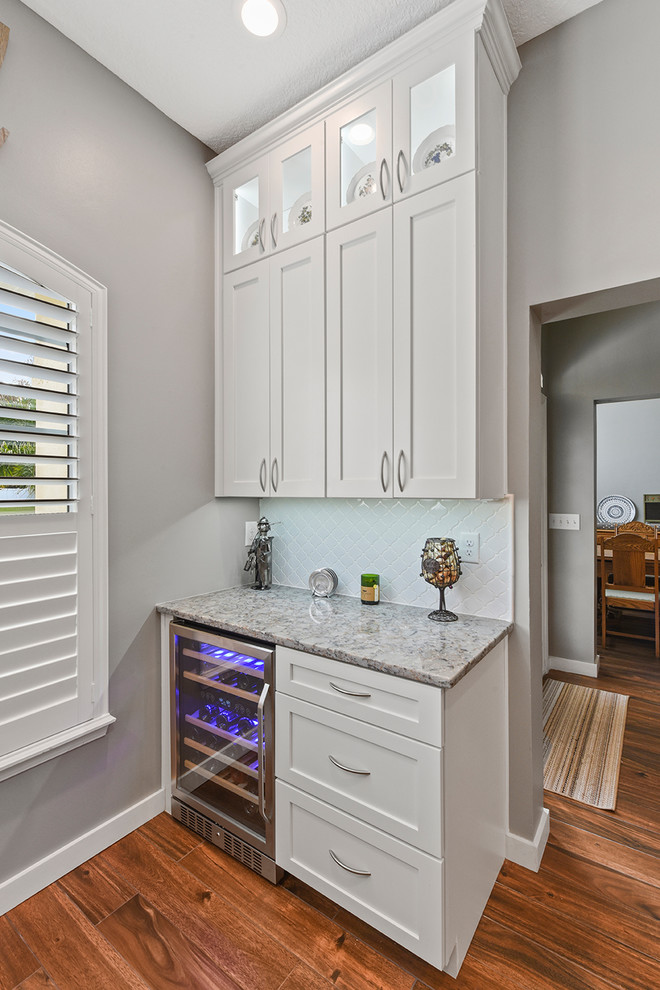Photo of a large contemporary u-shaped kitchen pantry in Jacksonville with a farmhouse sink, shaker cabinets, white cabinets, quartzite benchtops, white splashback, porcelain splashback, stainless steel appliances, porcelain floors, with island and brown floor.