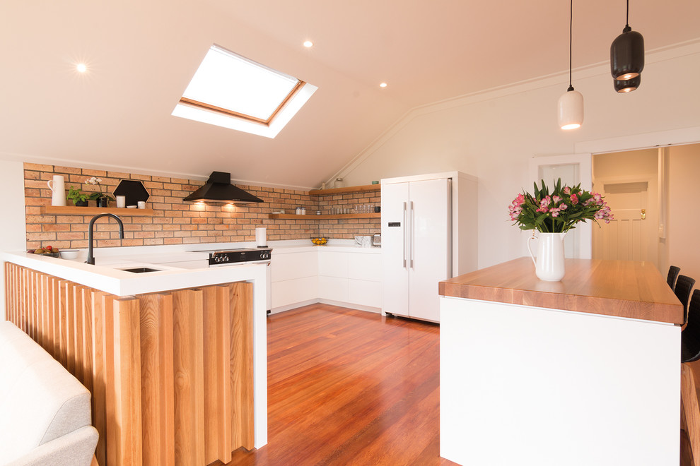 This is an example of a contemporary u-shaped kitchen in Melbourne with an undermount sink, flat-panel cabinets, white cabinets, medium hardwood floors, with island, brown floor and white benchtop.