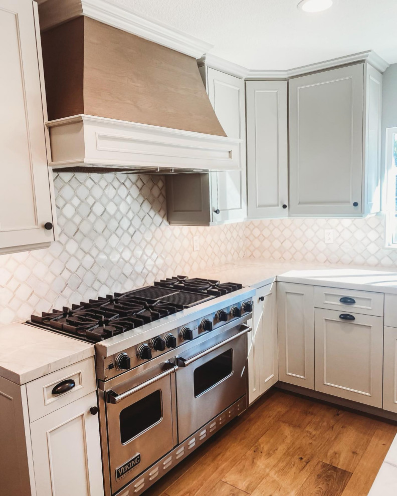 Klassisk inredning av ett mellanstort vit vitt kök med öppen planlösning, med en rustik diskho, luckor med infälld panel, skåp i ljust trä, bänkskiva i kvartsit, vitt stänkskydd, stänkskydd i mosaik, integrerade vitvaror, ljust trägolv, en köksö och brunt golv
