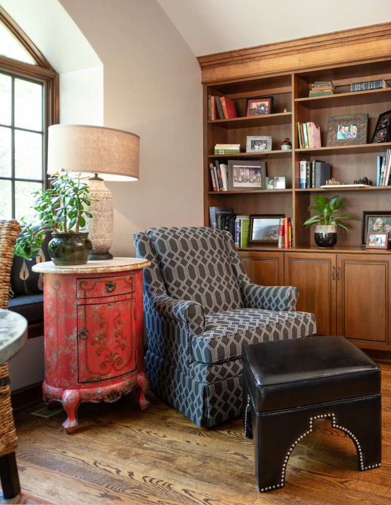 Exemple d'une salle de séjour éclectique avec une bibliothèque ou un coin lecture, un sol en bois brun, une cheminée standard, un manteau de cheminée en carrelage et poutres apparentes.