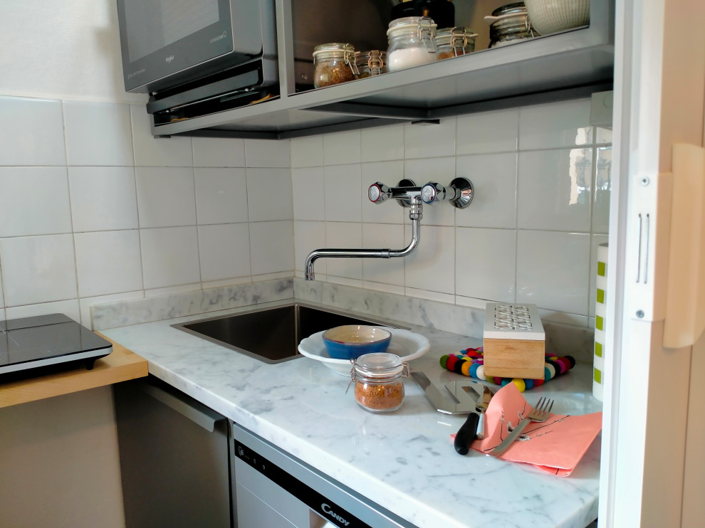 Foto på ett litet funkis vit linjärt kök med öppen planlösning, med en nedsänkt diskho, luckor med lamellpanel, grå skåp, marmorbänkskiva, vitt stänkskydd, stänkskydd i keramik, rostfria vitvaror, terrazzogolv och flerfärgat golv