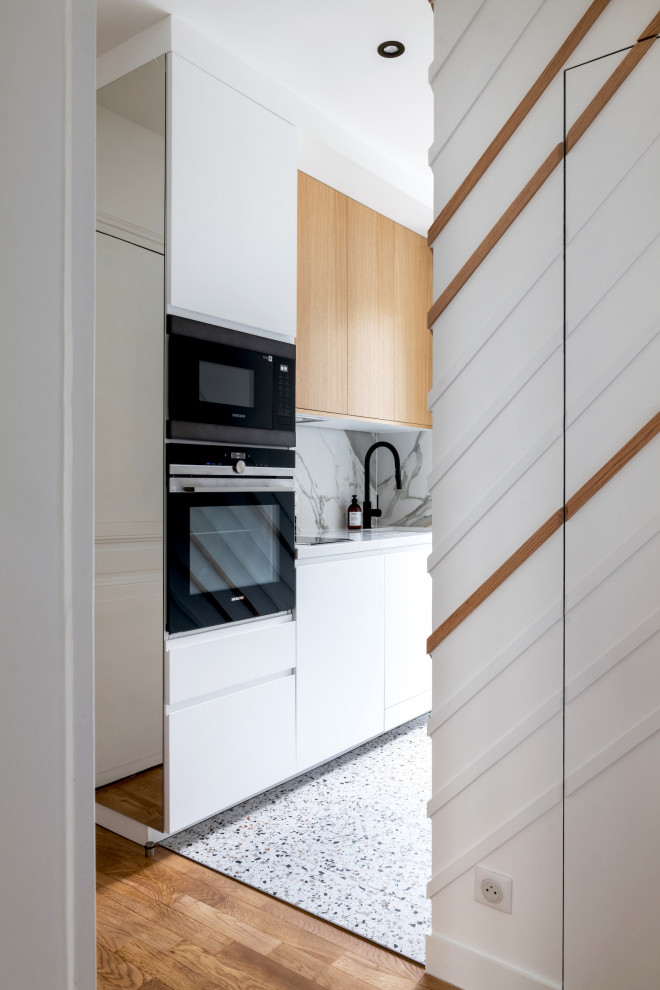 パリにある高級な中くらいなトラディショナルスタイルのおしゃれなキッチン (一体型シンク、白いキャビネット、珪岩カウンター、セラミックタイルのキッチンパネル、黒い調理設備、テラゾーの床、白いキッチンカウンター) の写真