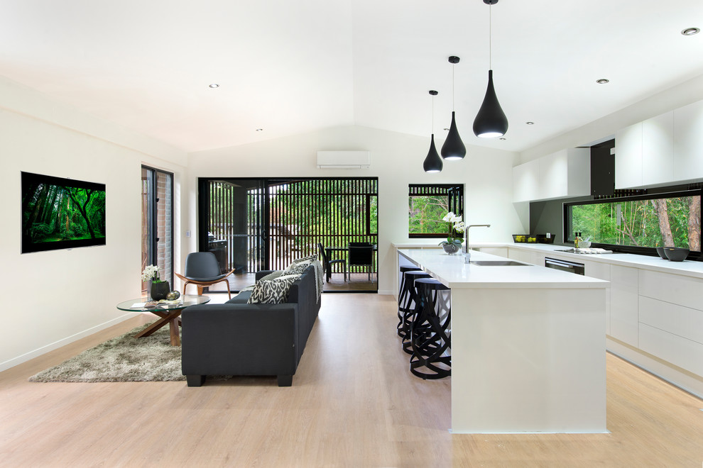 Design ideas for a contemporary galley open plan kitchen in Brisbane with an undermount sink, flat-panel cabinets, white cabinets, window splashback, black appliances, light hardwood floors, with island, beige floor and white benchtop.