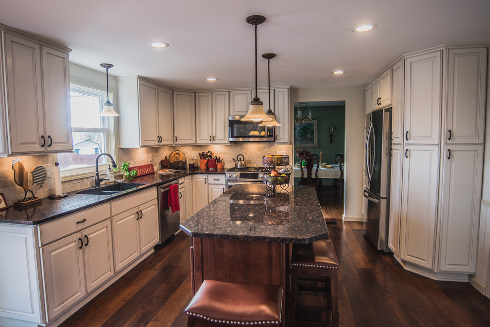 This is an example of a mid-sized traditional l-shaped eat-in kitchen in New York with a double-bowl sink, raised-panel cabinets, white cabinets, quartz benchtops, beige splashback, stainless steel appliances, dark hardwood floors, with island and brown floor.