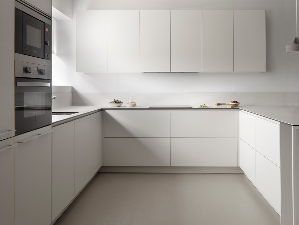 This is an example of a mid-sized contemporary u-shaped separate kitchen in Other with an undermount sink, flat-panel cabinets, white cabinets, solid surface benchtops, white splashback, stainless steel appliances and no island.