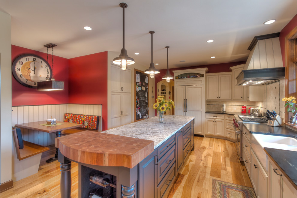 Mountain style l-shaped medium tone wood floor eat-in kitchen photo with a farmhouse sink, raised-panel cabinets, white cabinets, granite countertops, white backsplash, ceramic backsplash, paneled appliances and an island