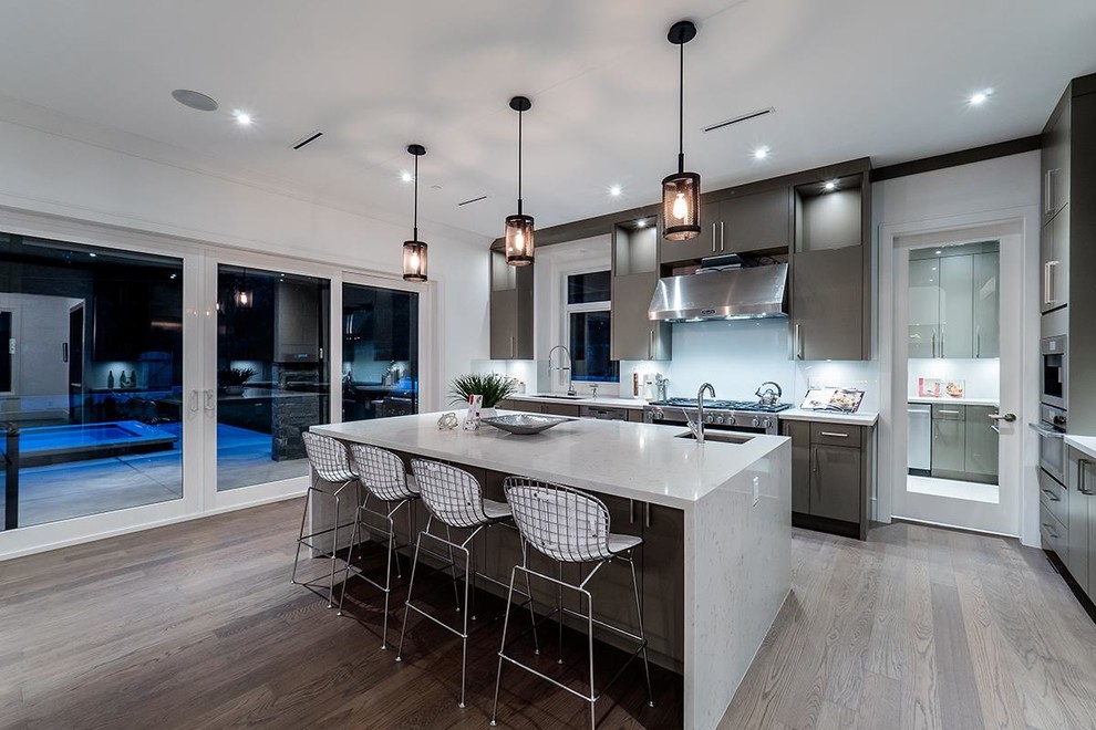 Photo of a contemporary galley kitchen in Vancouver with an undermount sink, flat-panel cabinets, grey cabinets, glass sheet splashback, stainless steel appliances, light hardwood floors and with island.