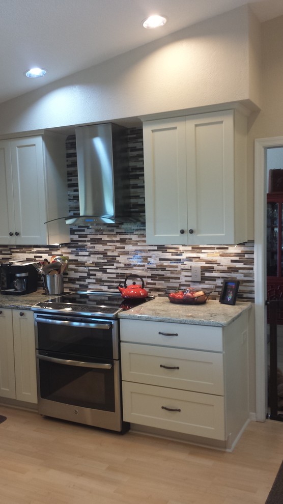 Open concept kitchen - mid-sized transitional u-shaped light wood floor open concept kitchen idea in Phoenix with a single-bowl sink, flat-panel cabinets, white cabinets, granite countertops, brown backsplash, glass tile backsplash, stainless steel appliances and a peninsula