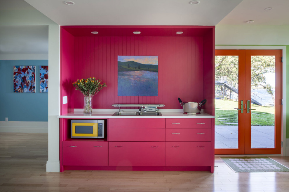 This is an example of an eclectic single-wall kitchen in Minneapolis with a double-bowl sink, flat-panel cabinets, pink cabinets, pink splashback, shiplap splashback, coloured appliances, light hardwood floors and white benchtop.