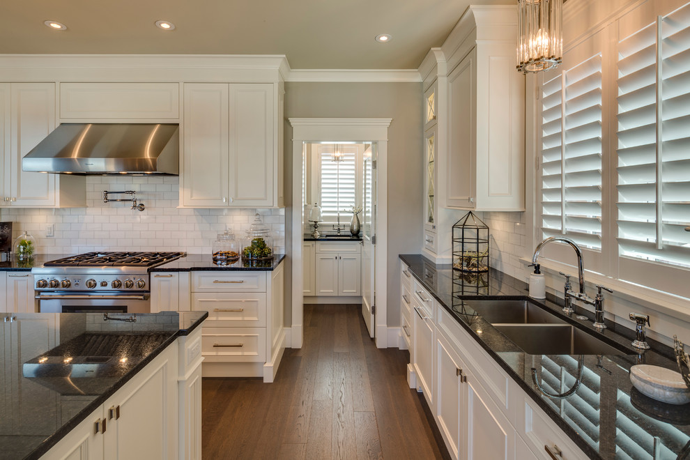 Inspiration for a mid-sized traditional l-shaped eat-in kitchen in Vancouver with an undermount sink, recessed-panel cabinets, white cabinets, granite benchtops, white splashback, subway tile splashback, stainless steel appliances and with island.