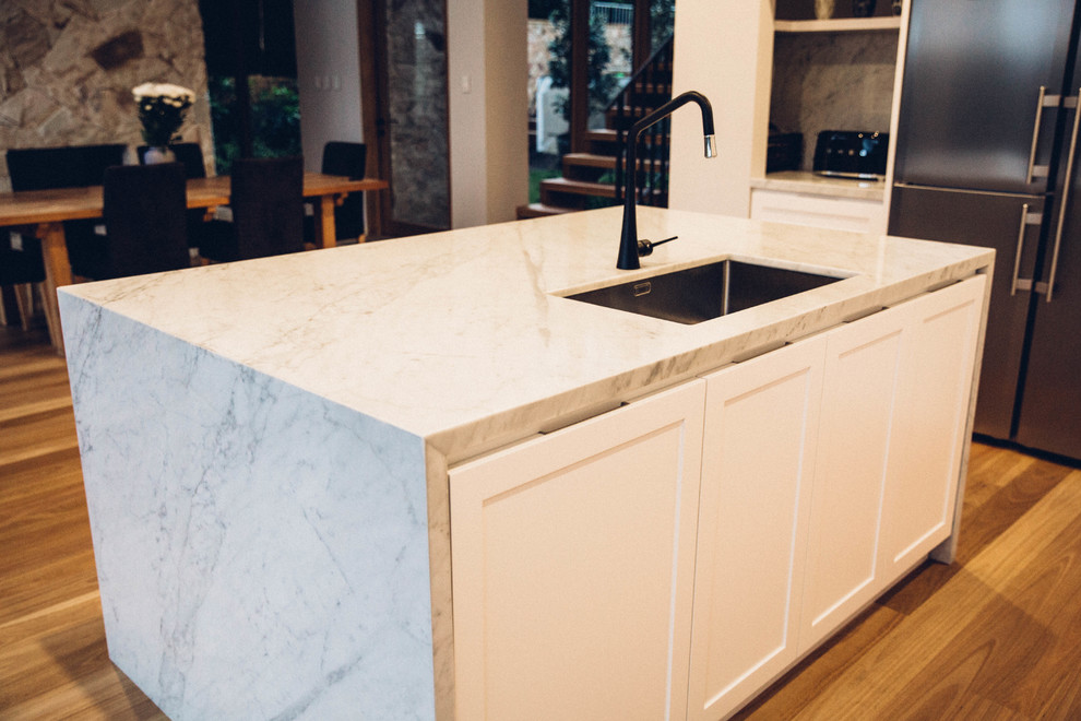 Inspiration for a contemporary l-shaped open plan kitchen in Sydney with white cabinets, marble benchtops, grey splashback, stone slab splashback, stainless steel appliances, medium hardwood floors, with island, an undermount sink and recessed-panel cabinets.