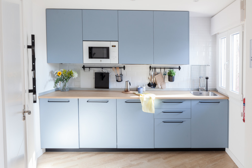 Photo of a small scandinavian single-wall open plan kitchen in Other with a belfast sink, flat-panel cabinets, blue cabinets, laminate countertops, white splashback, ceramic splashback, white appliances, laminate floors, no island, brown floors and brown worktops.