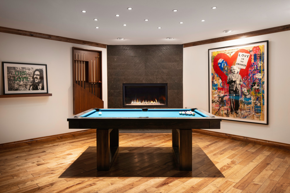 This is an example of an expansive fully buried basement in Denver with a game room, white walls, medium hardwood floors, a stone fireplace surround, brown floor, wood and a corner fireplace.
