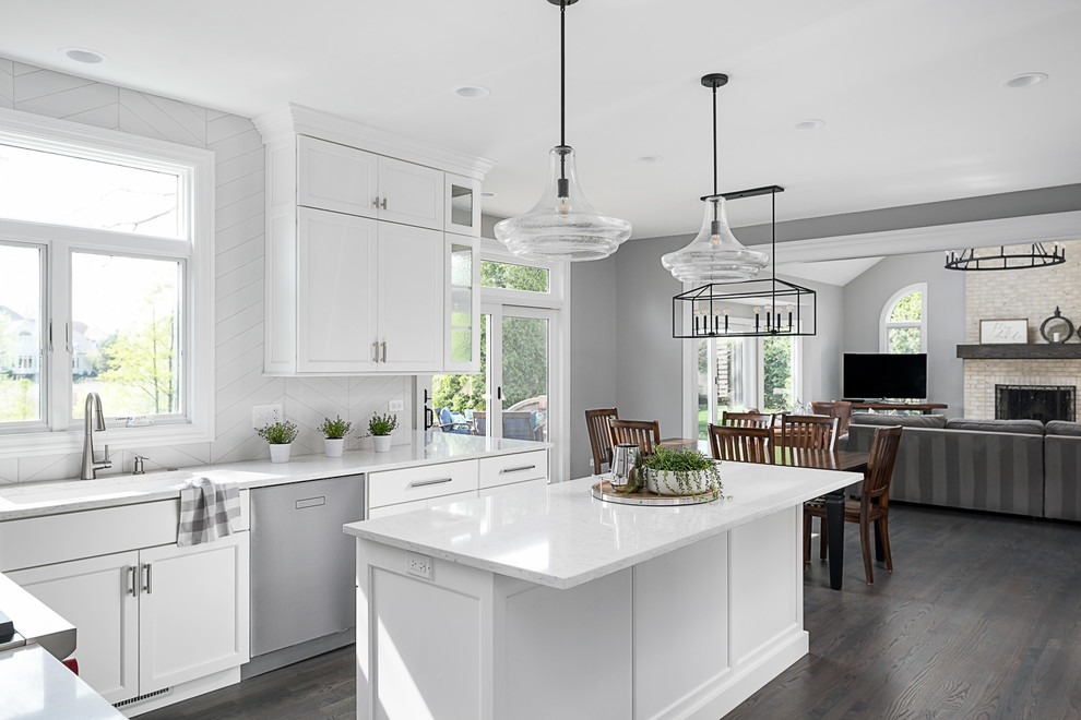 Photo of a large transitional u-shaped eat-in kitchen in Chicago with white cabinets, white splashback, porcelain splashback, stainless steel appliances, light hardwood floors, with island, grey floor and white benchtop.