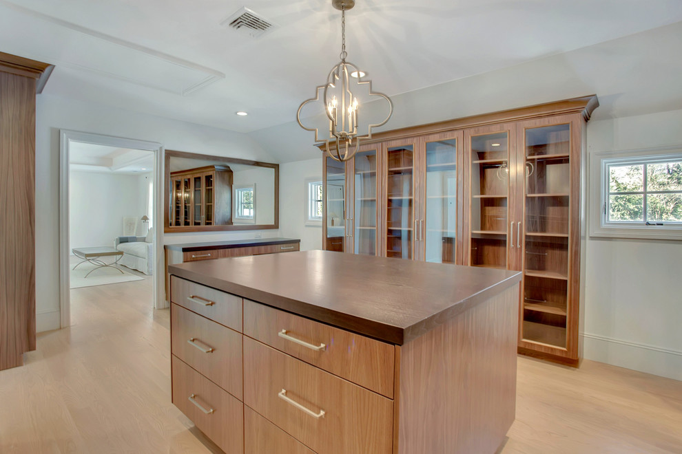 Photo of an expansive transitional gender-neutral built-in wardrobe in New York with glass-front cabinets, medium wood cabinets, light hardwood floors and brown floor.