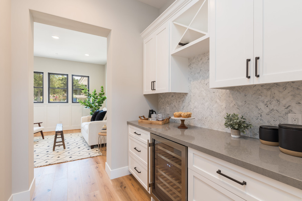 This is an example of a mid-sized country galley eat-in kitchen in San Luis Obispo with a farmhouse sink, recessed-panel cabinets, white cabinets, marble benchtops, white splashback, stone tile splashback, stainless steel appliances, with island, white benchtop, light hardwood floors and beige floor.