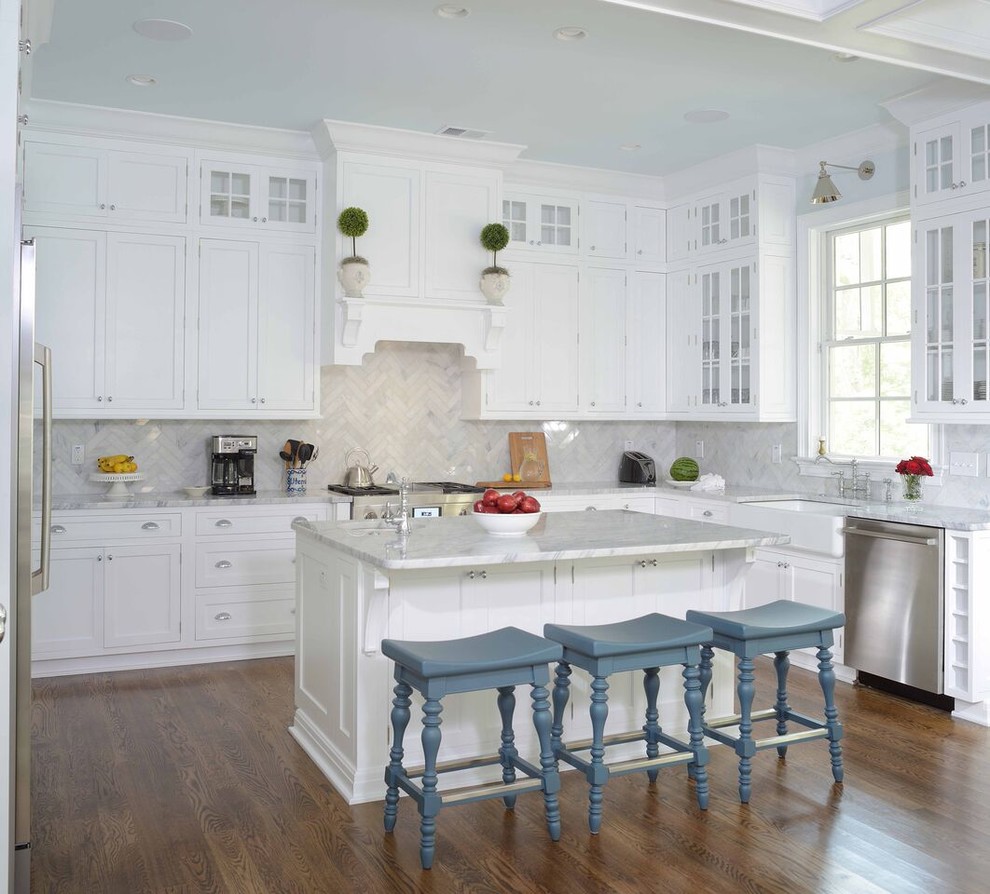 Photo of a traditional l-shaped kitchen in Charleston with a farmhouse sink, shaker cabinets, white cabinets, white splashback, stainless steel appliances, dark hardwood floors and with island.