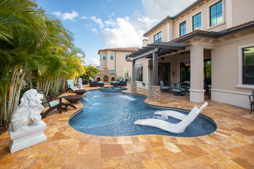 Photo of a mid-sized mediterranean backyard custom-shaped pool in Miami with a water feature and natural stone pavers.