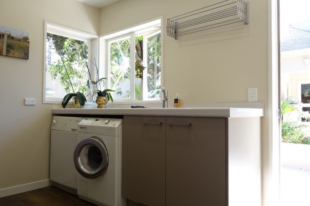 Contemporary galley utility room in Auckland with an undermount sink, flat-panel cabinets, laminate benchtops, white walls, ceramic floors, a side-by-side washer and dryer and grey cabinets.