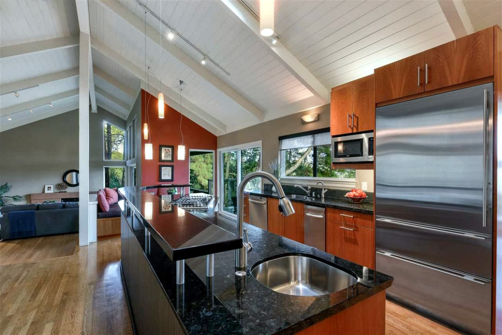 This is an example of a mid-sized contemporary l-shaped eat-in kitchen in San Francisco with an undermount sink, flat-panel cabinets, dark wood cabinets, granite benchtops, glass sheet splashback, stainless steel appliances, medium hardwood floors, with island, brown floor, black benchtop, exposed beam, vaulted and wood.