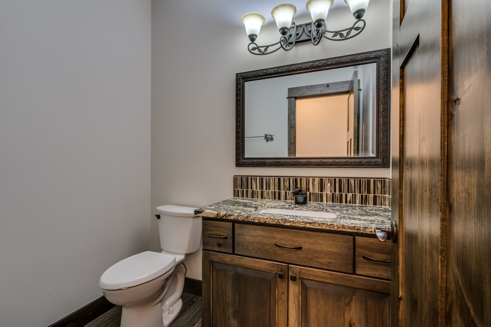 Photo of a small country powder room in Other with raised-panel cabinets, medium wood cabinets, a one-piece toilet, beige tile, ceramic tile, beige walls, laminate floors, an undermount sink, engineered quartz benchtops and beige floor.