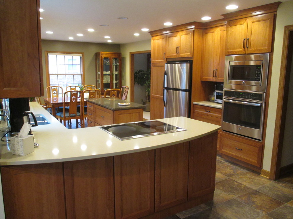 Mid-sized transitional u-shaped slate floor eat-in kitchen photo with an undermount sink, recessed-panel cabinets, medium tone wood cabinets, stainless steel appliances, solid surface countertops and a peninsula